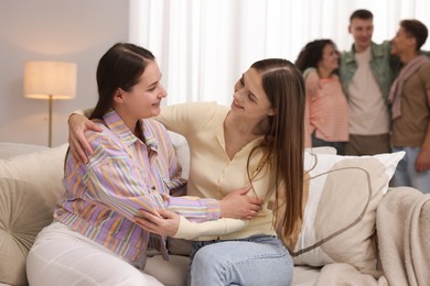 Photo of Friends hugging on sofa indoors, selective focus