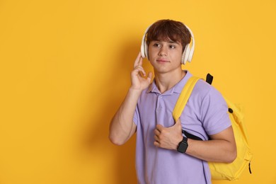 Photo of Cute teenage boy with backpack and headphones on yellow background. Space for text