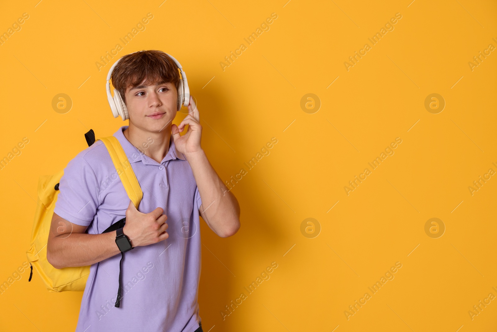 Cute teenage boy with backpack and headphones on yellow background. Space for text Photo of Cute teenage boy with backpack and headphones on yellow background. Space for text
