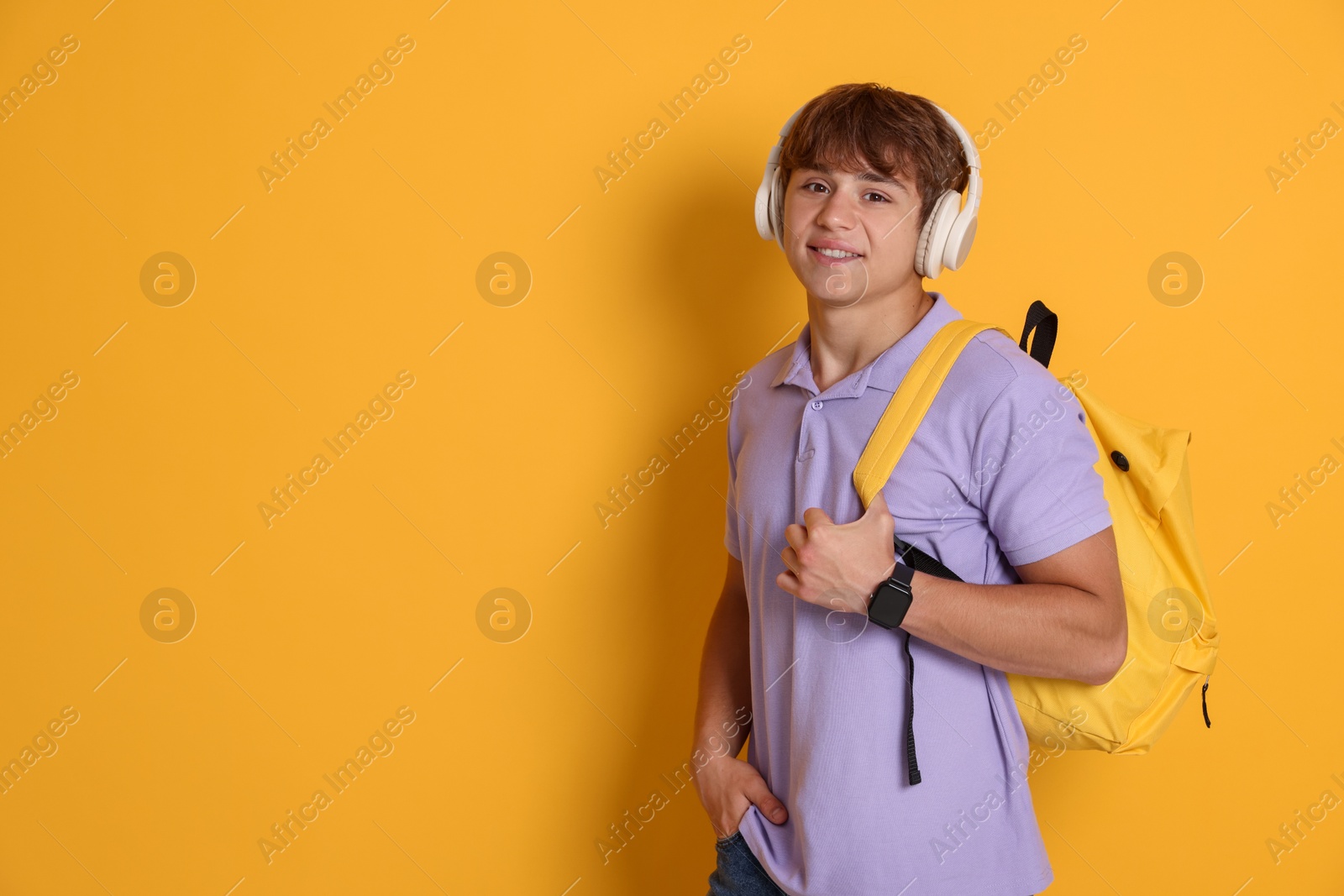 Smiling teenage boy with backpack and headphones on yellow background. Space for text Photo of Smiling teenage boy with backpack and headphones on yellow background. Space for text