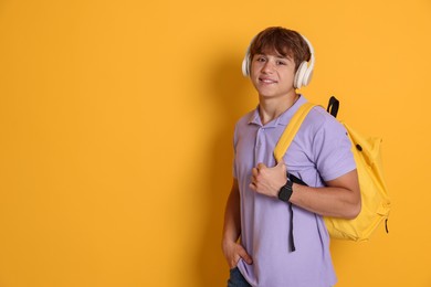 Photo of Smiling teenage boy with backpack and headphones on yellow background. Space for text