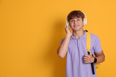 Photo of Smiling teenage boy with backpack and headphones on yellow background. Space for text