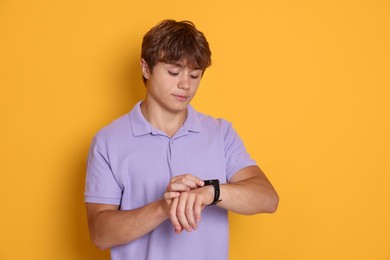 Photo of Cute teenage boy looking at wristwatch on yellow background
