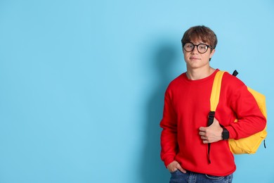 Photo of Cute teenage boy in glasses with backpack on light blue background. Space for text