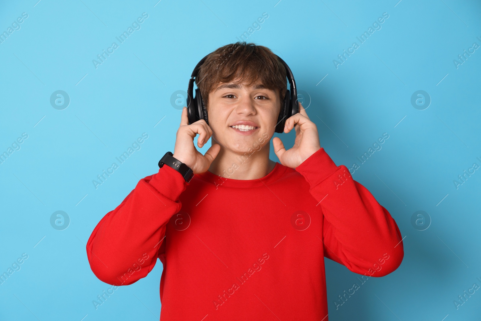 Portrait of smiling teenage boy in headphones on light blue background Photo of Portrait of smiling teenage boy in headphones on light blue background