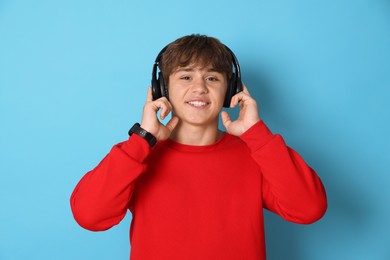 Photo of Portrait of smiling teenage boy in headphones on light blue background