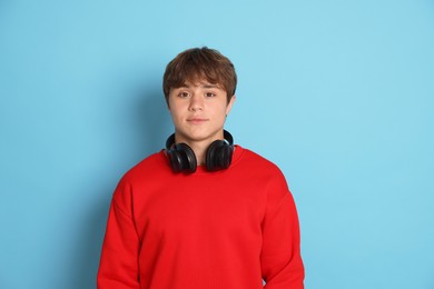 Photo of Portrait of cute teenage boy with headphones on light blue background