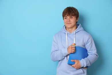 Photo of Cute teenage boy with book on light blue background. Space for text