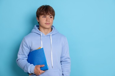 Photo of Cute teenage boy with book on light blue background. Space for text