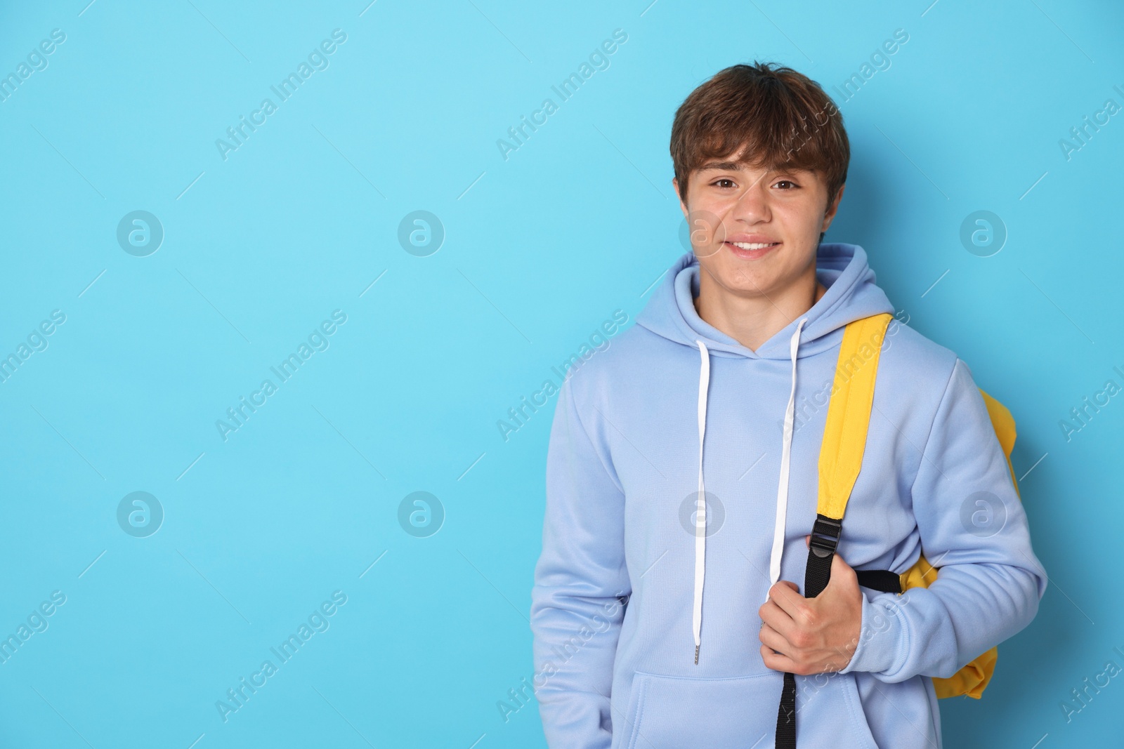 Portrait of smiling teenage boy with backpack on light blue background. Space for text Photo of Portrait of smiling teenage boy with backpack on light blue background. Space for text