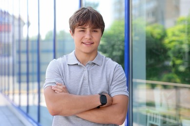 Photo of Portrait of smiling teenage boy with crossed arms near building outdoors