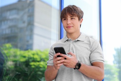Photo of Cute teenage boy with smartphone near building outdoors