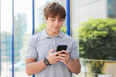 Photo of Cute teenage boy with smartphone near building outdoors