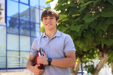 Photo of Smiling teenage boy with books on city street, low angle view