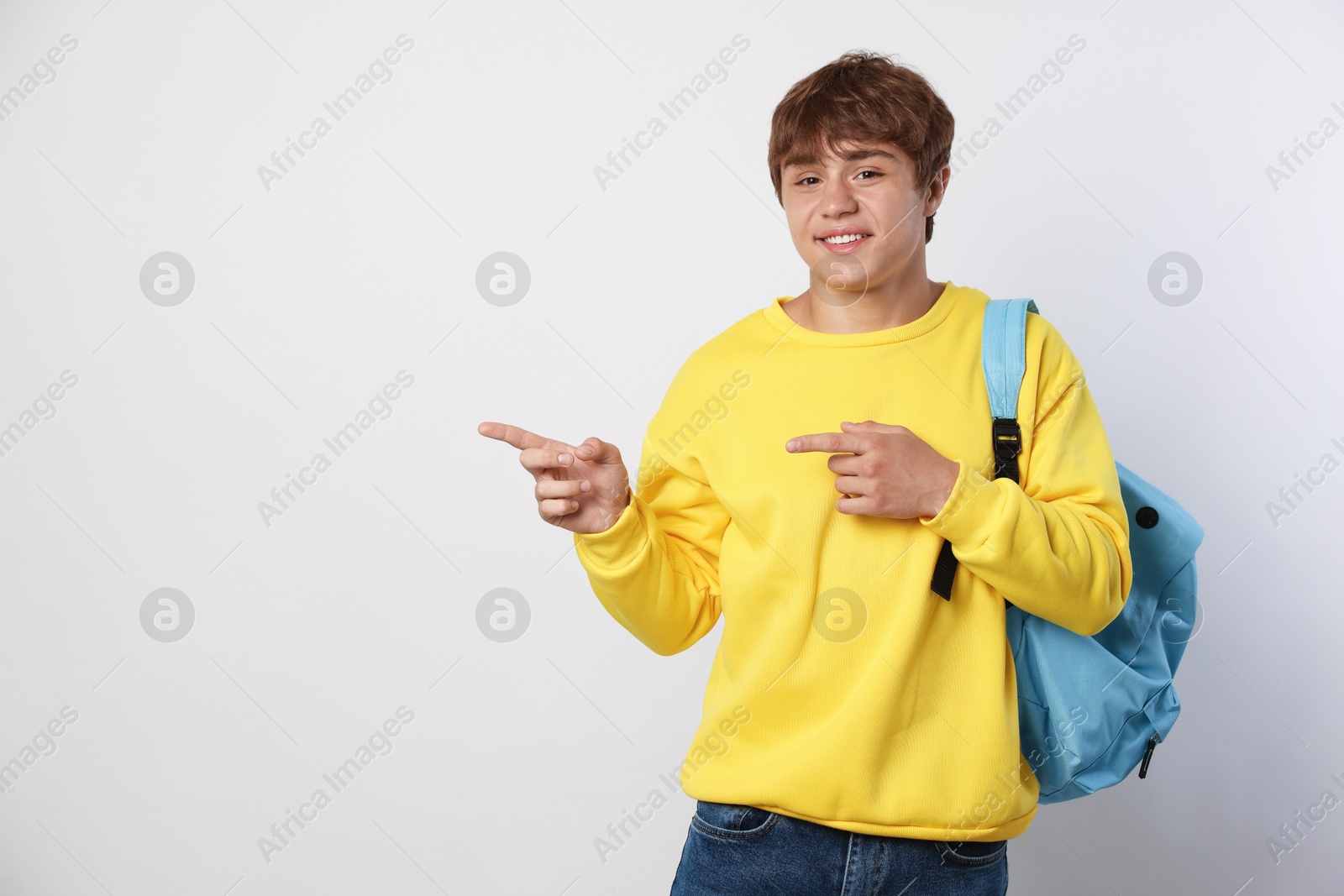 Smiling teenage boy with backpack pointing at something on light grey background. Space for text Photo of Smiling teenage boy with backpack pointing at something on light grey background. Space for text