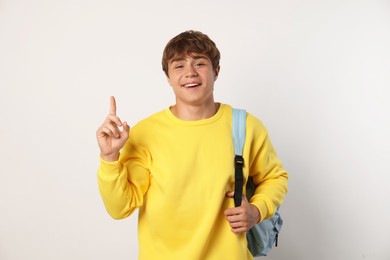 Photo of Smiling teenage boy with backpack pointing upwards on light grey background