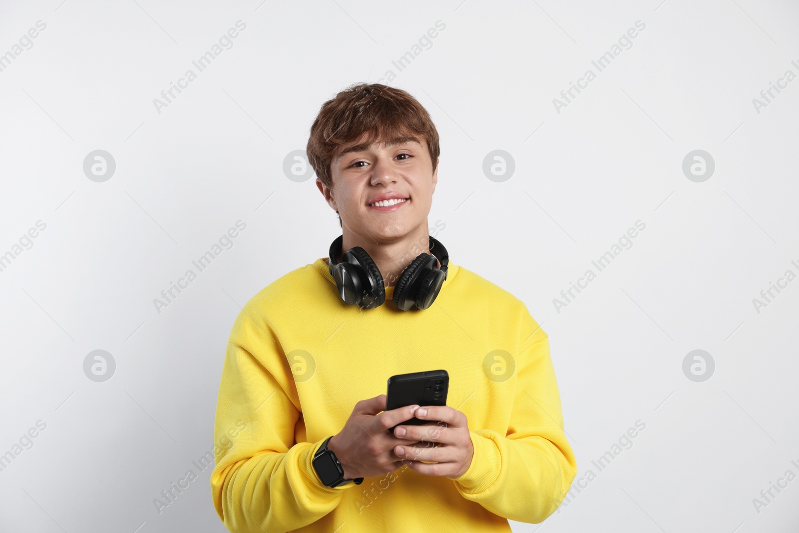 Portrait of smiling teenage boy with headphones and smartphone on light grey background Photo of Portrait of smiling teenage boy with headphones and smartphone on light grey background