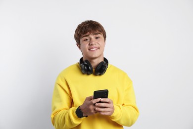 Photo of Portrait of smiling teenage boy with headphones and smartphone on light grey background