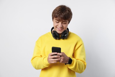 Photo of Smiling teenage boy with headphones and smartphone on light grey background