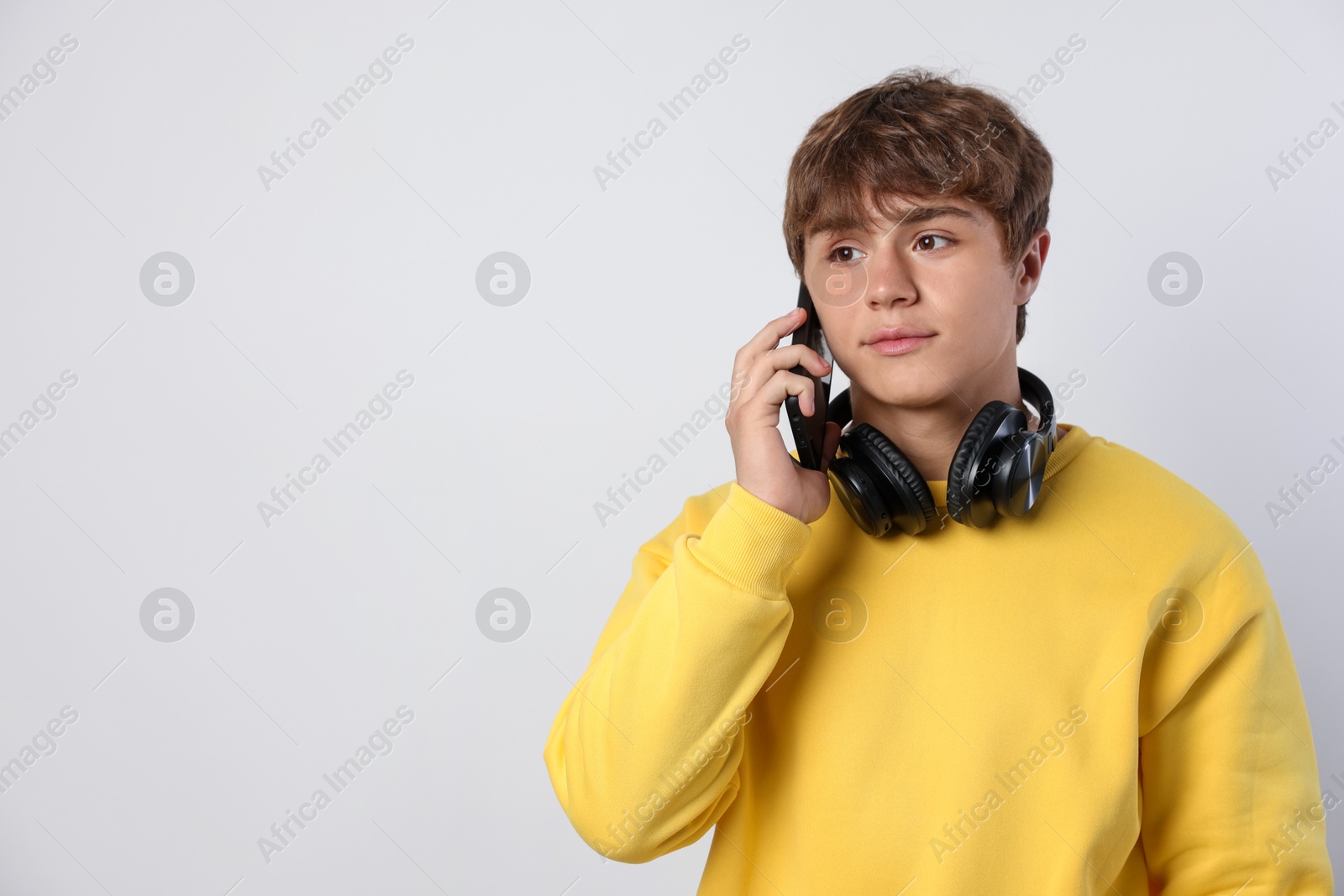 Cute teenage boy with headphones talking by smartphone on light grey background. Space for text Photo of Cute teenage boy with headphones talking by smartphone on light grey background. Space for text