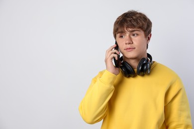 Photo of Cute teenage boy with headphones talking by smartphone on light grey background. Space for text