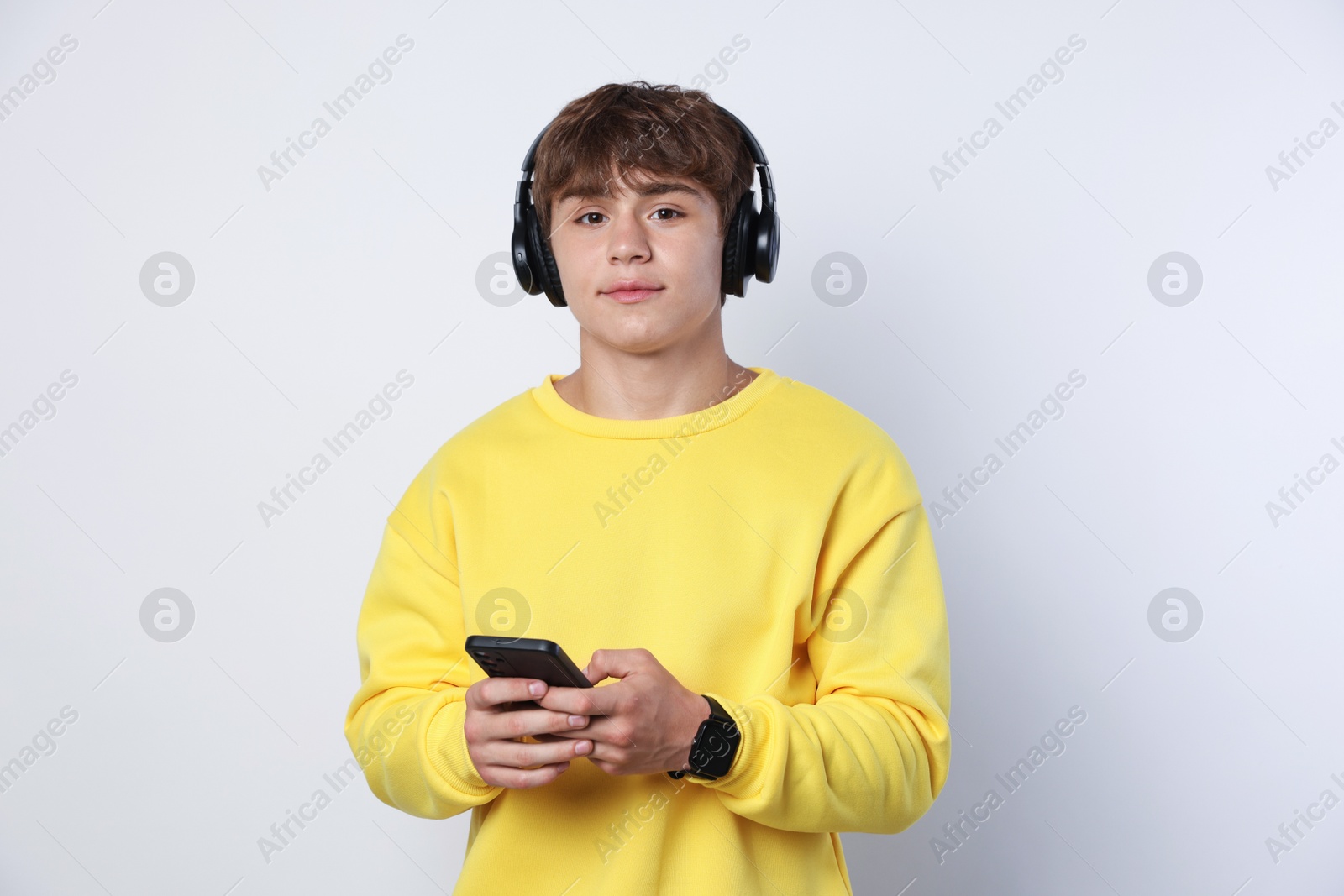 Portrait of cute teenage boy in headphones with smartphone on light grey background Photo of Portrait of cute teenage boy in headphones with smartphone on light grey background