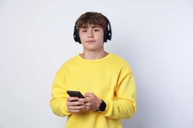Photo of Portrait of cute teenage boy in headphones with smartphone on light grey background