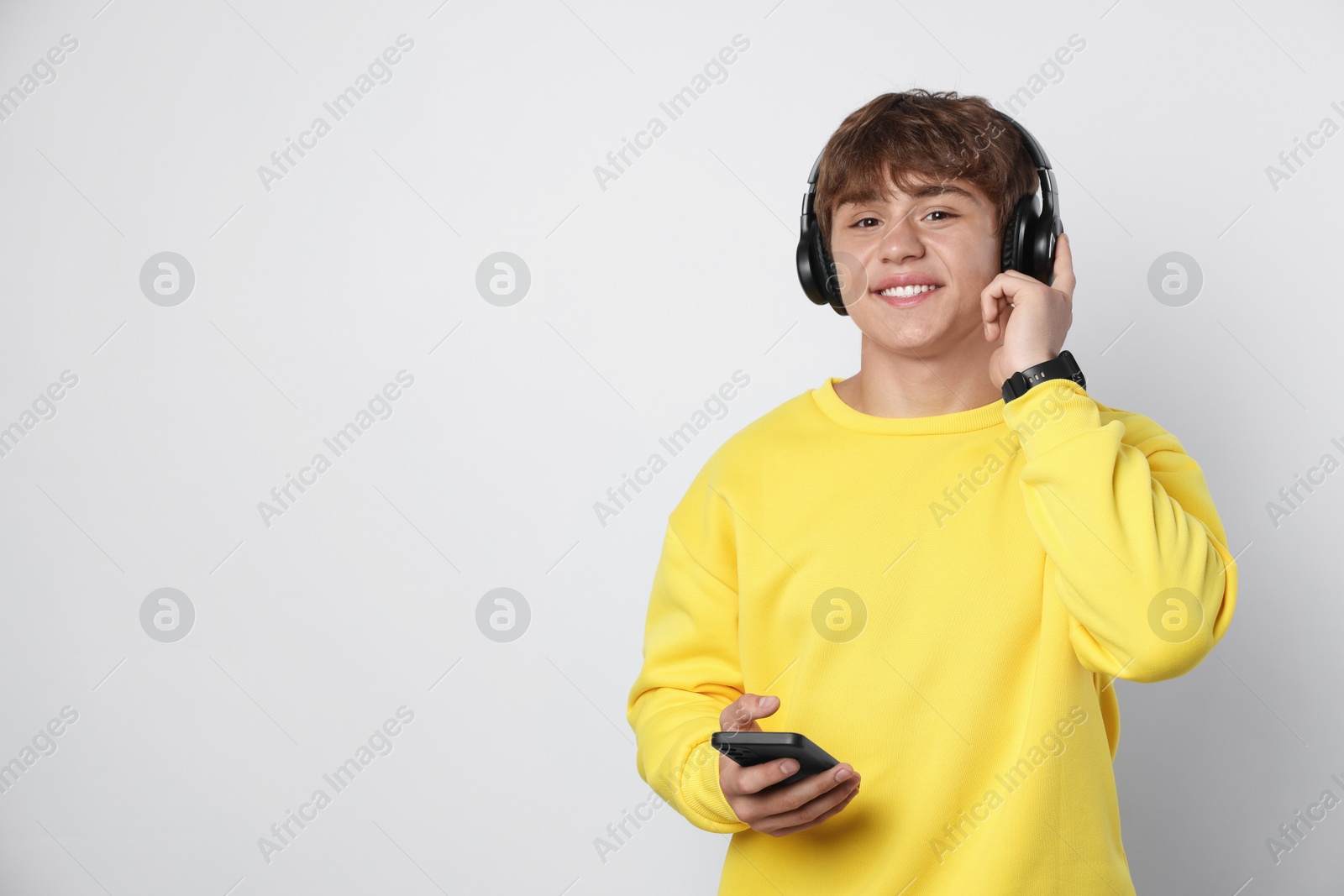 Portrait of smiling teenage boy in headphones with smartphone on light grey background. Space for text Photo of Portrait of smiling teenage boy in headphones with smartphone on light grey background. Space for text