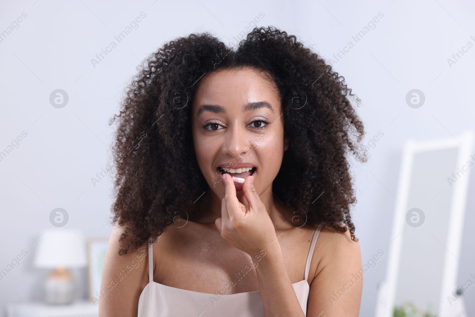 Beautiful Brazilian woman taking collagen pill indoors Photo of Beautiful Brazilian woman taking collagen pill indoors