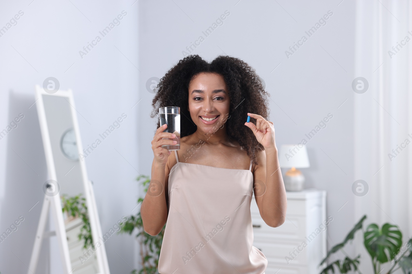 Beautiful Brazilian woman with glass of water and collagen pill indoors Photo of Beautiful Brazilian woman with glass of water and collagen pill indoors