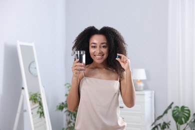 Photo of Beautiful Brazilian woman with glass of water and collagen pill indoors
