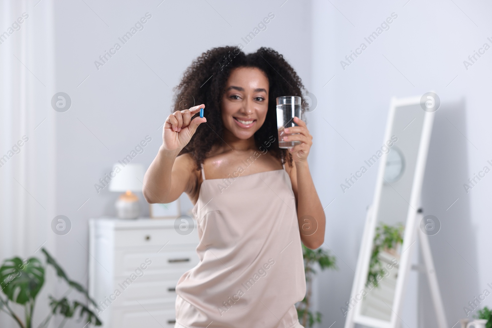 Beautiful Brazilian woman with glass of water and collagen pill indoors Photo of Beautiful Brazilian woman with glass of water and collagen pill indoors