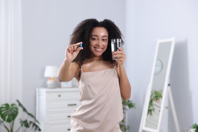 Photo of Beautiful Brazilian woman with glass of water and collagen pill indoors