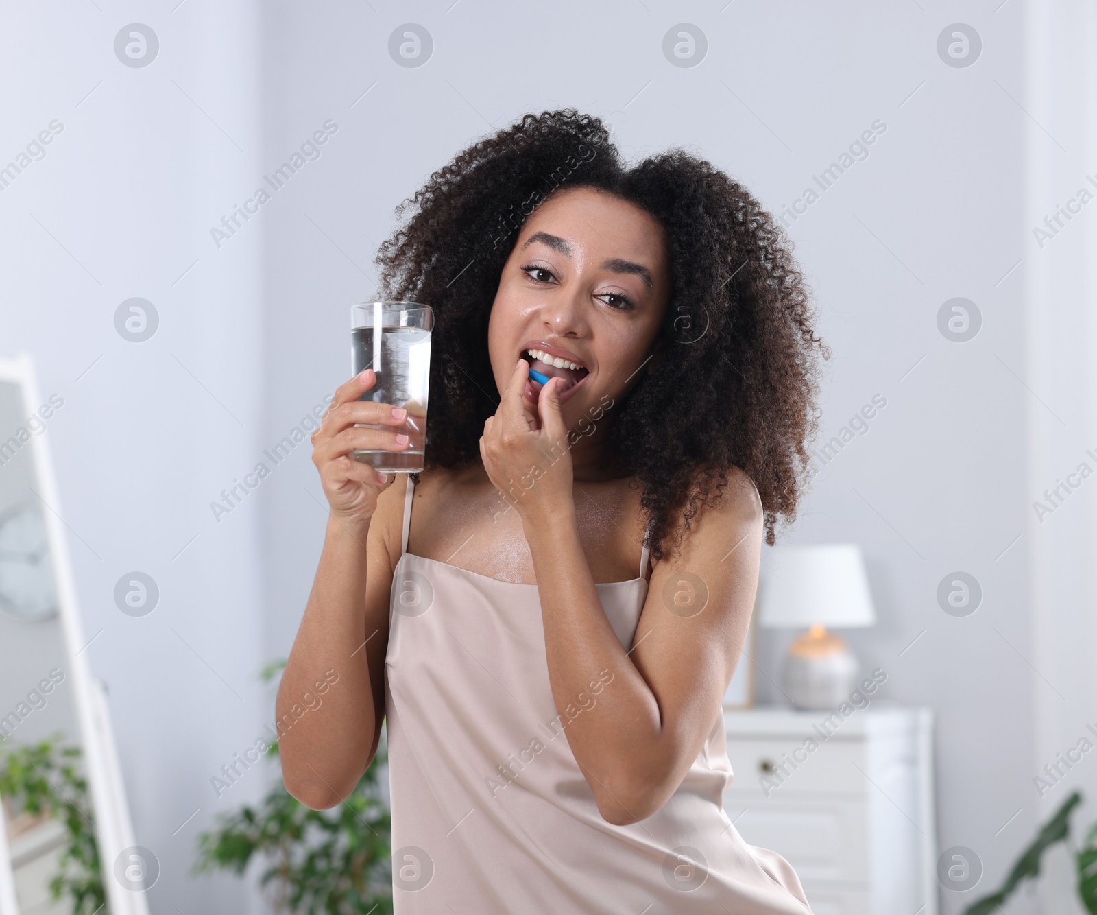 Beautiful Brazilian woman with glass of water taking collagen pill indoors Photo of Beautiful Brazilian woman with glass of water taking collagen pill indoors
