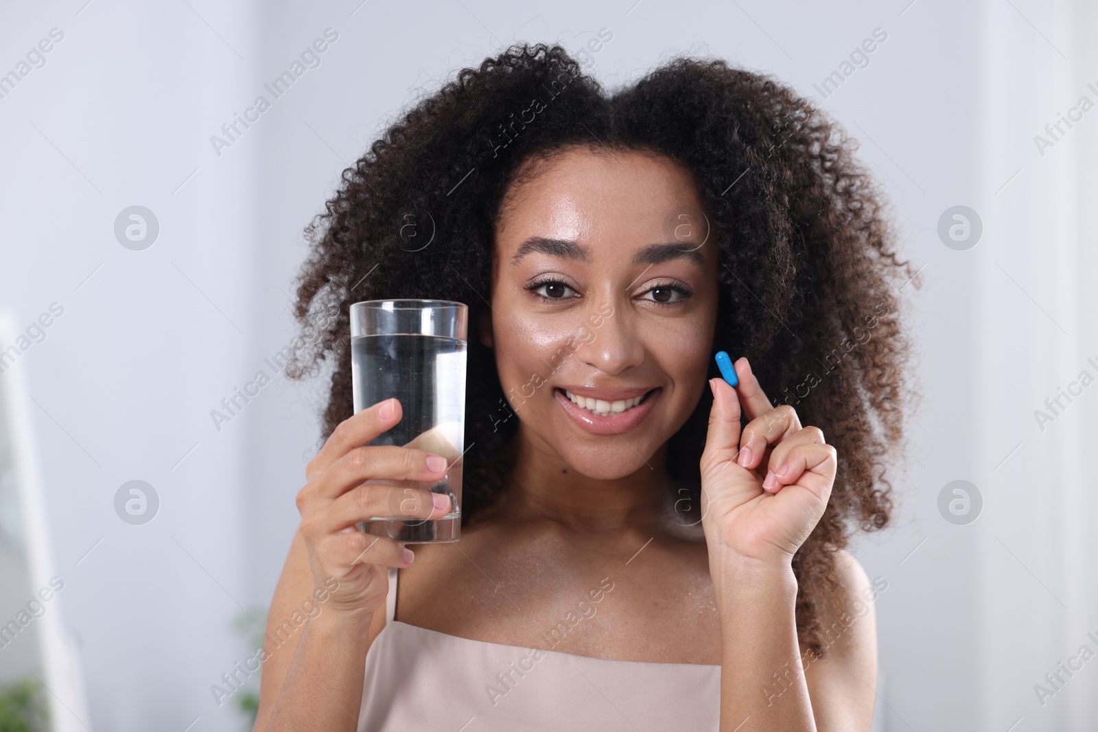 Beautiful Brazilian woman with glass of water and collagen pill indoors Photo of Beautiful Brazilian woman with glass of water and collagen pill indoors