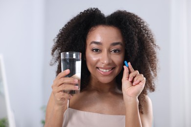 Photo of Beautiful Brazilian woman with glass of water and collagen pill indoors