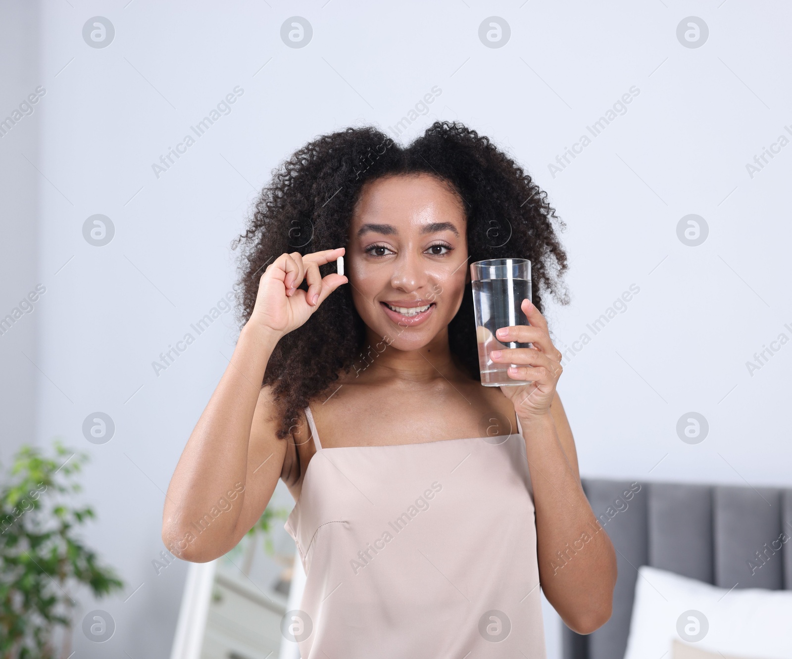 Beautiful Brazilian woman with glass of water and collagen pill indoors Photo of Beautiful Brazilian woman with glass of water and collagen pill indoors