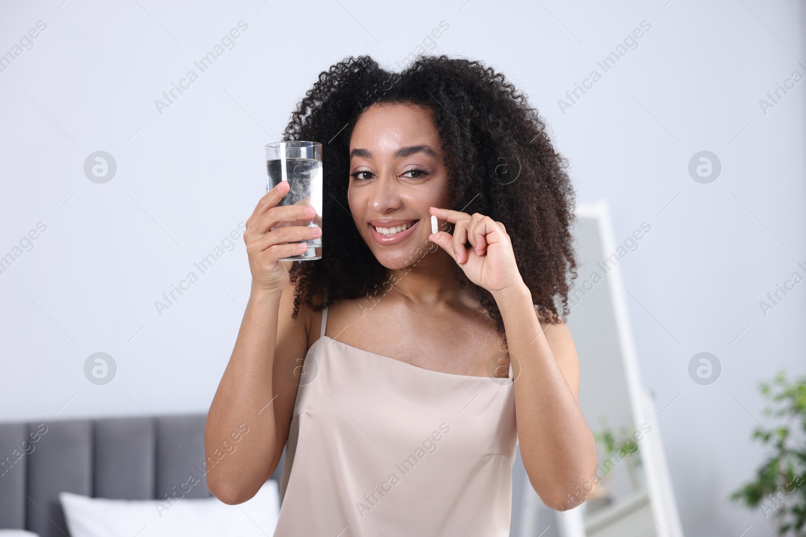 Beautiful Brazilian woman with glass of water and collagen pill indoors Photo of Beautiful Brazilian woman with glass of water and collagen pill indoors