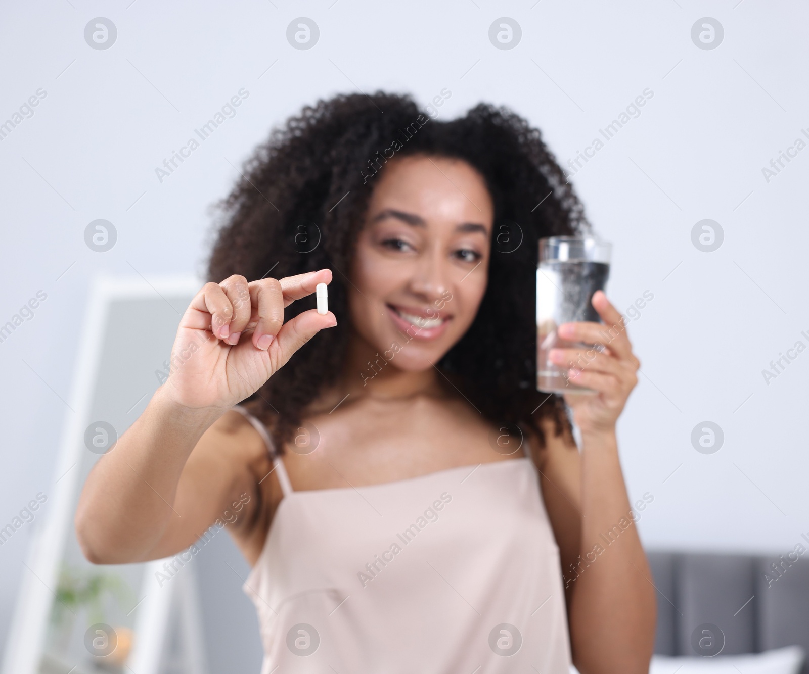 Beautiful Brazilian woman with glass of water and collagen pill indoors, selective focus Photo of Beautiful Brazilian woman with glass of water and collagen pill indoors, selective focus