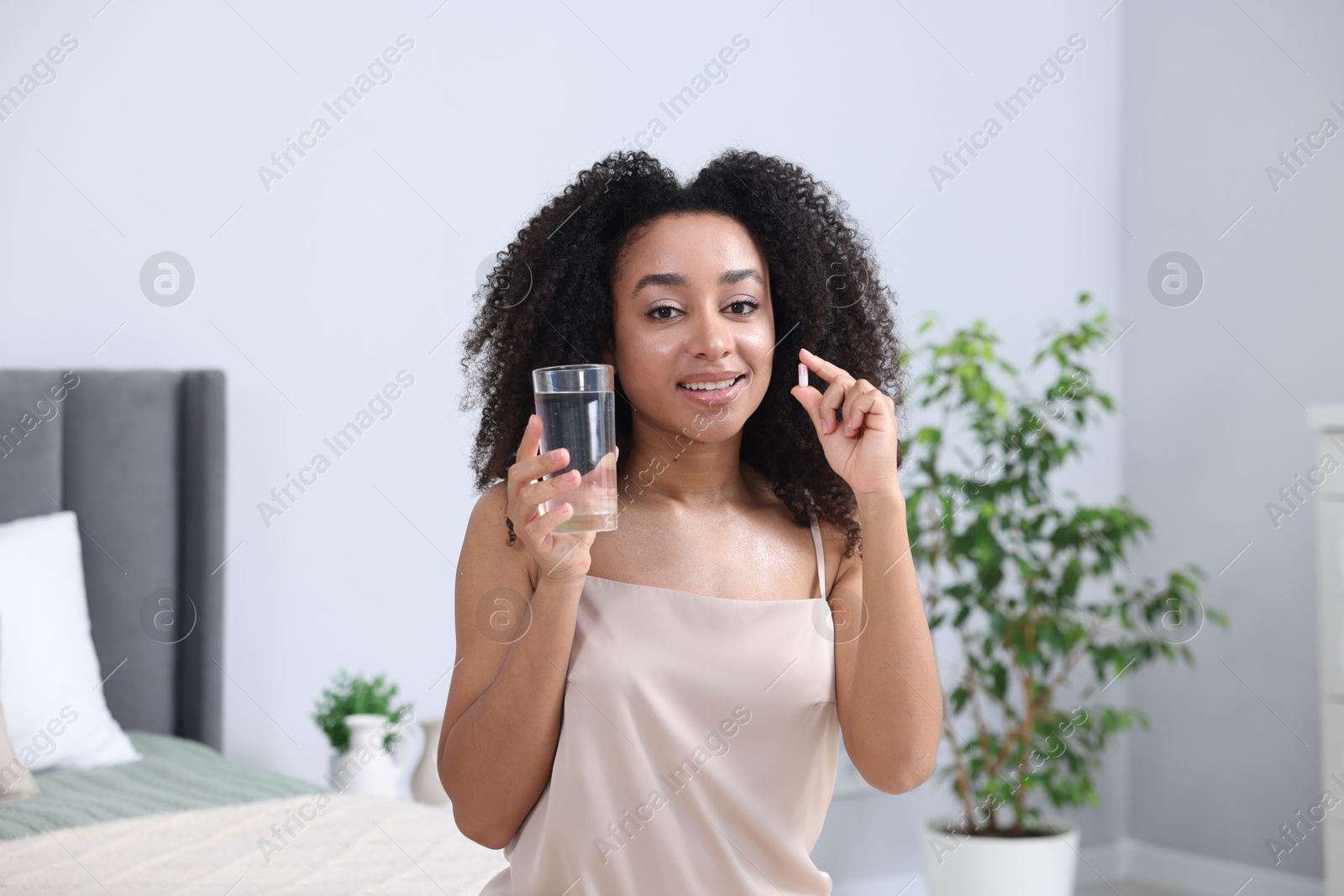 Beautiful Brazilian woman with glass of water and collagen pill indoors Photo of Beautiful Brazilian woman with glass of water and collagen pill indoors