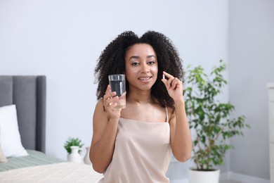 Photo of Beautiful Brazilian woman with glass of water and collagen pill indoors