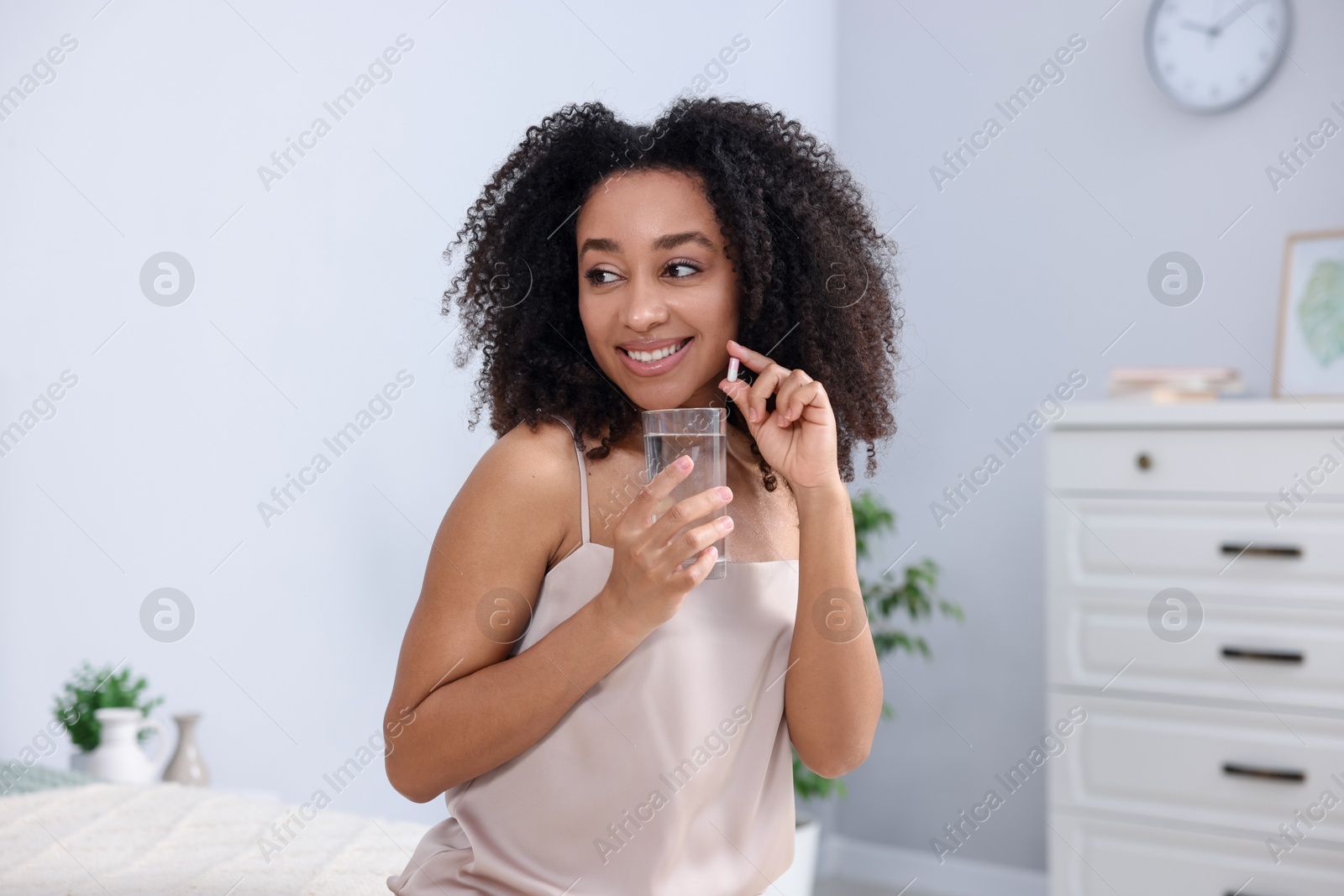 Beautiful Brazilian woman with glass of water and collagen pill indoors Photo of Beautiful Brazilian woman with glass of water and collagen pill indoors