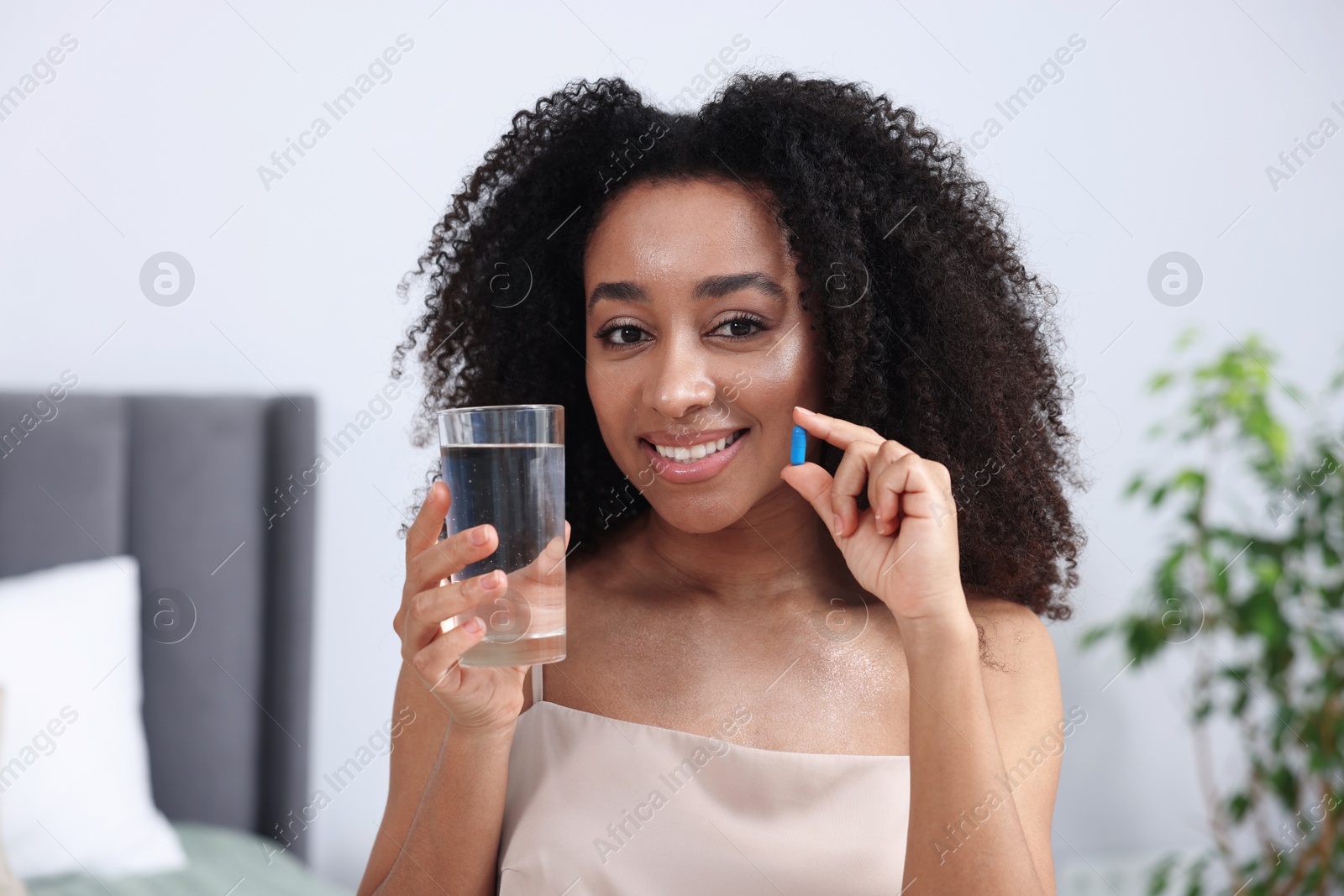 Beautiful Brazilian woman with glass of water and collagen pill indoors Photo of Beautiful Brazilian woman with glass of water and collagen pill indoors