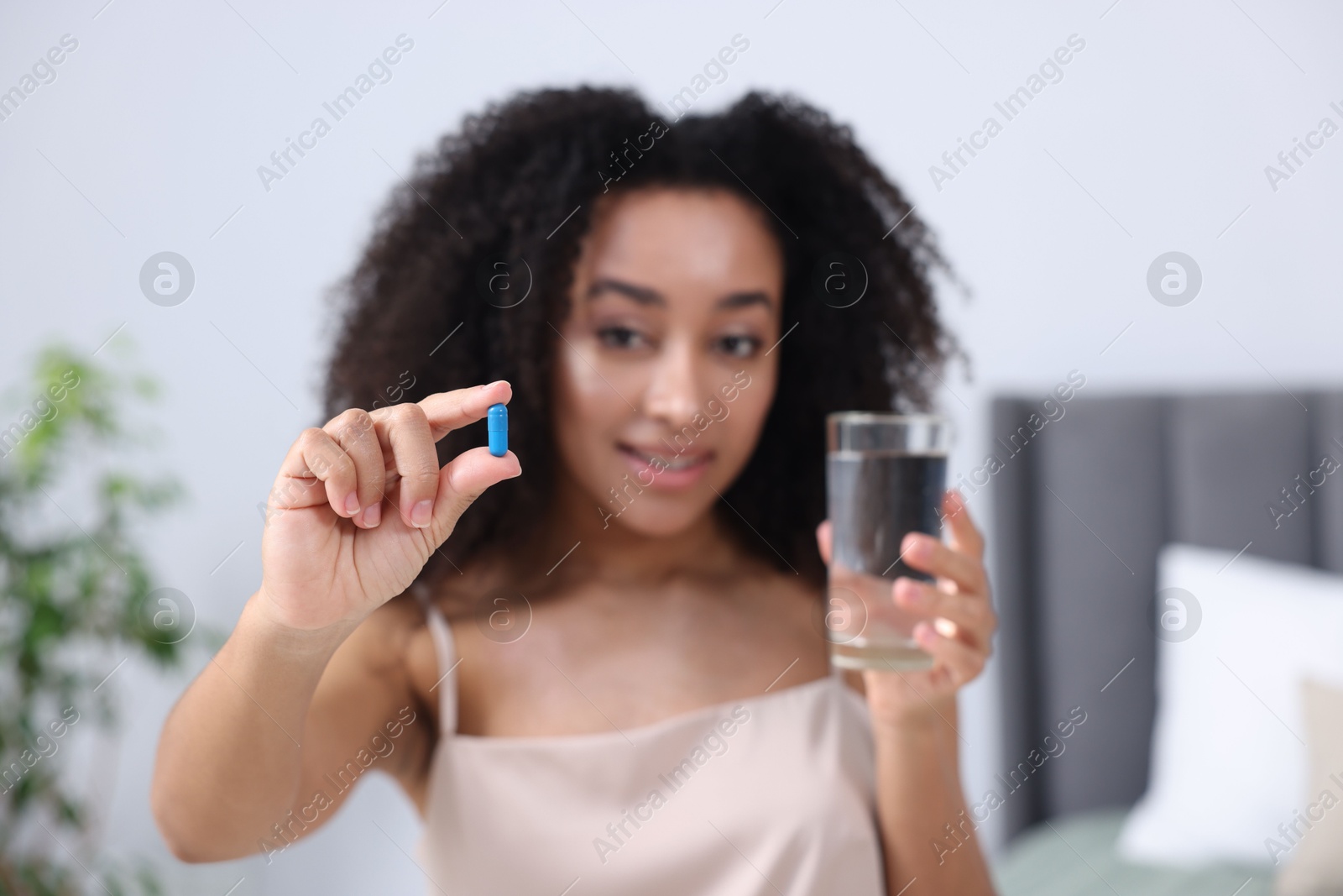 Beautiful Brazilian woman with glass of water and collagen pill indoors, selective focus Photo of Beautiful Brazilian woman with glass of water and collagen pill indoors, selective focus