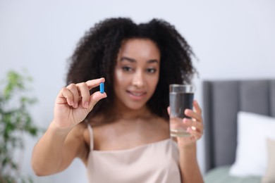 Photo of Beautiful Brazilian woman with glass of water and collagen pill indoors, selective focus