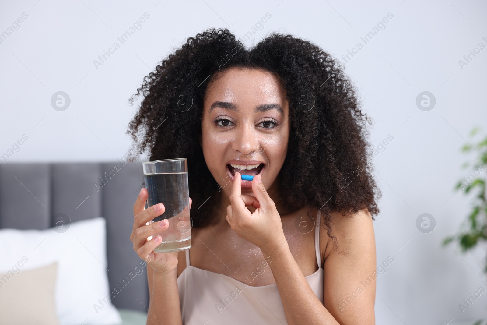 Beautiful Brazilian woman with glass of water taking collagen pill indoors Photo of Beautiful Brazilian woman with glass of water taking collagen pill indoors