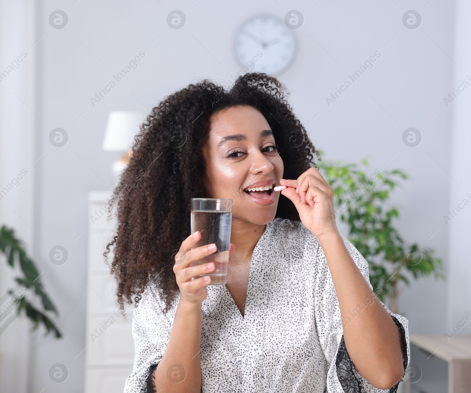 Beautiful Brazilian woman with glass of water and collagen pill indoors Photo of Beautiful Brazilian woman with glass of water and collagen pill indoors
