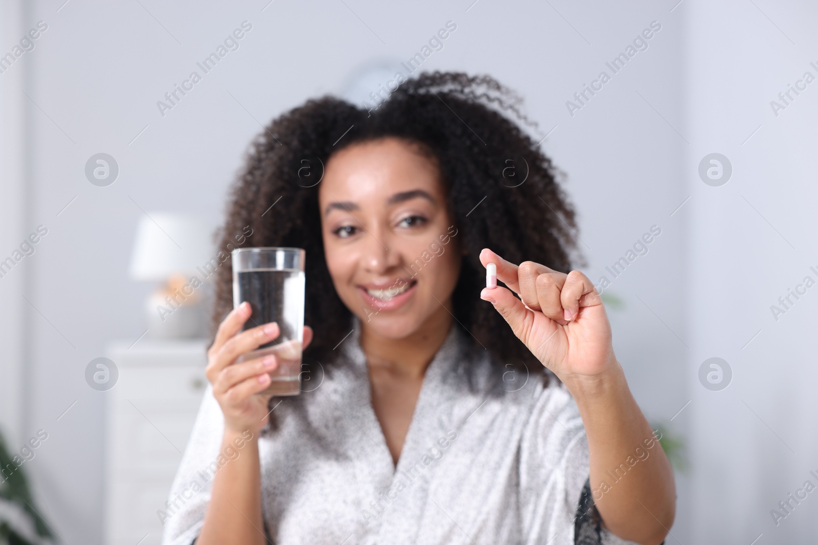 Beautiful Brazilian woman with glass of water and collagen pill indoors, selective focus Photo of Beautiful Brazilian woman with glass of water and collagen pill indoors, selective focus