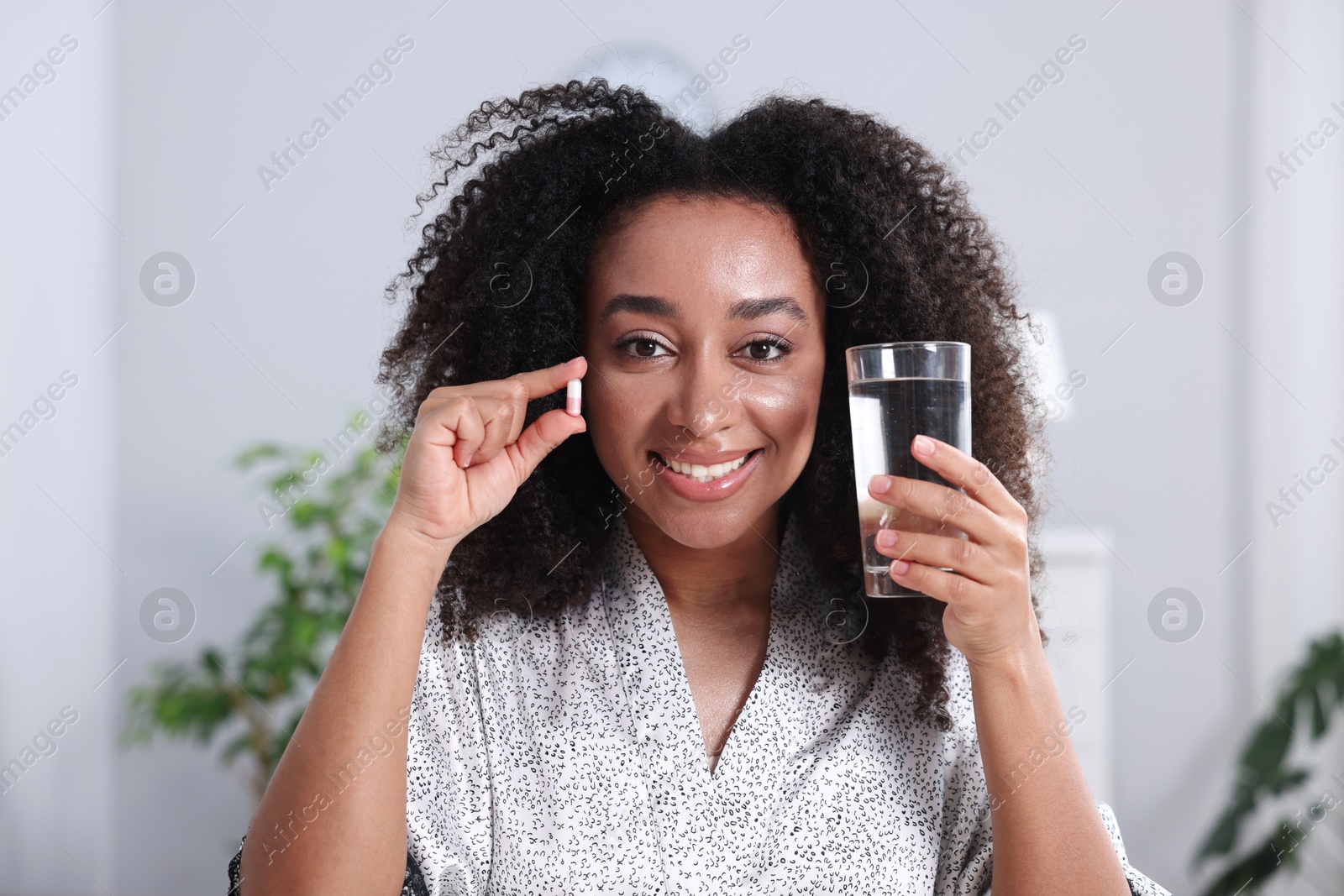 Beautiful Brazilian woman with glass of water and collagen pill indoors Photo of Beautiful Brazilian woman with glass of water and collagen pill indoors