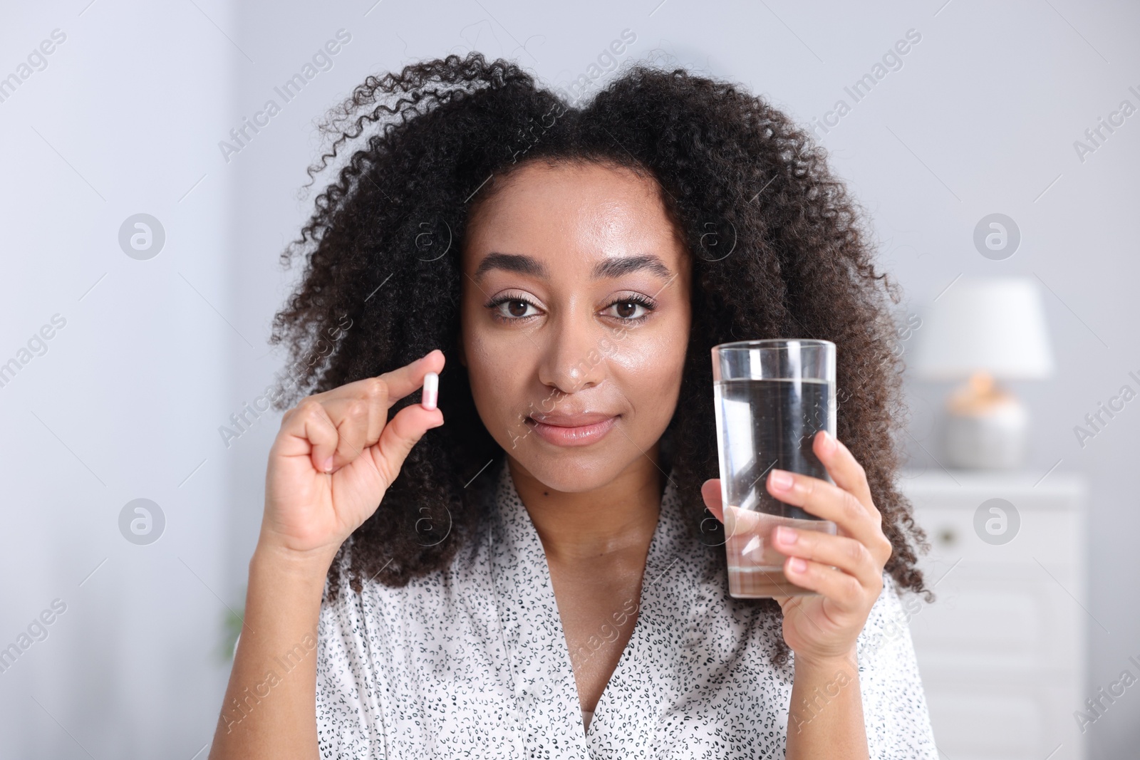 Beautiful Brazilian woman with glass of water and collagen pill indoors Photo of Beautiful Brazilian woman with glass of water and collagen pill indoors